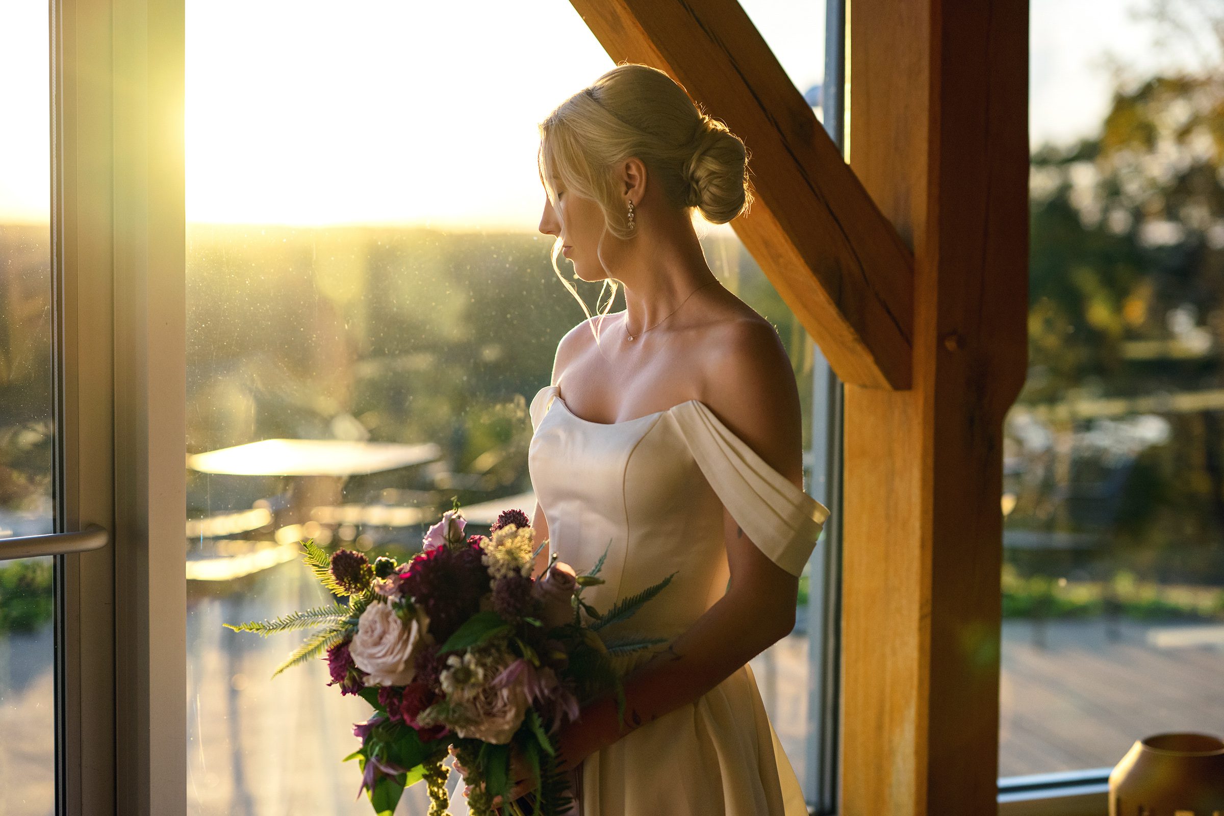 bride holding bouquet next to window at sunset