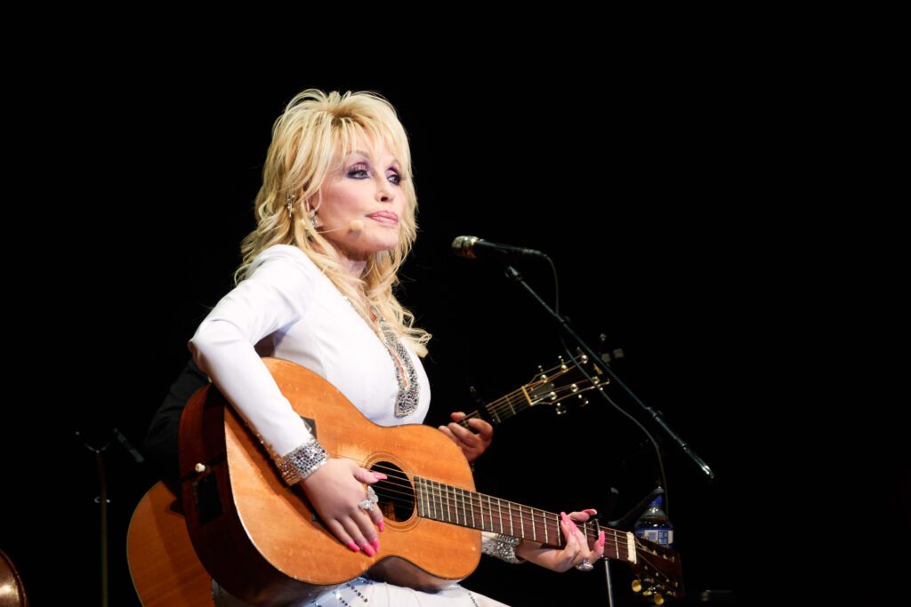 Dolly Parton sits on a coat of many colors quilt on stage at the Congress of Country Music