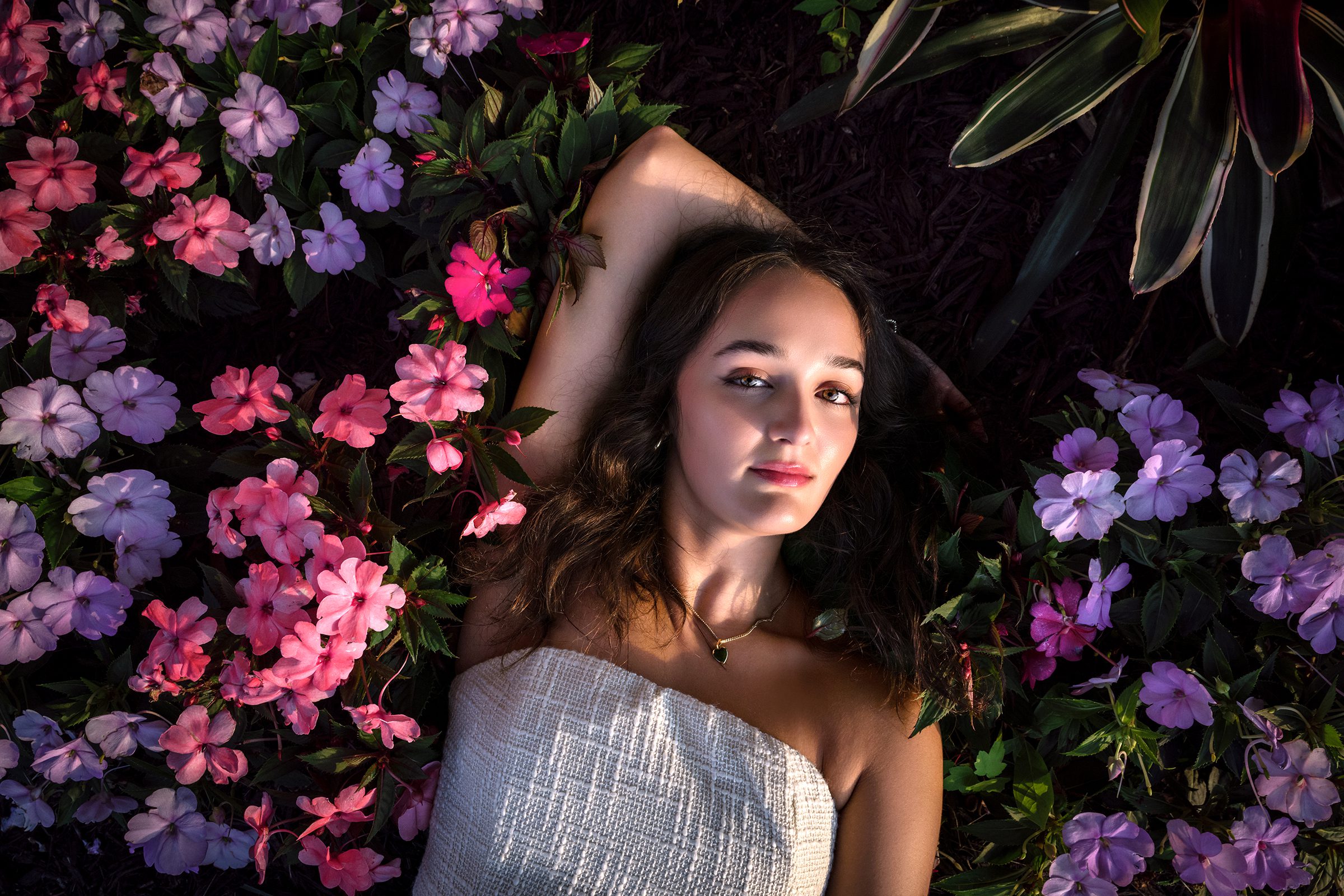 senior girl laying in pink and purple flowers with white dress