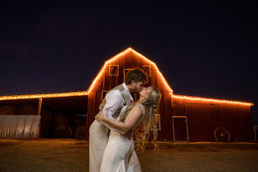 Bride and Groom kiss at night in front of sweet clover farms wedding barn