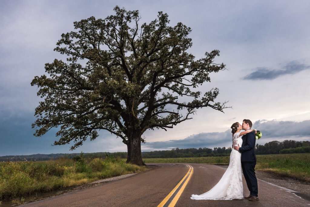 bride and groom kissing on the road in front of Big Tree McBain, MO