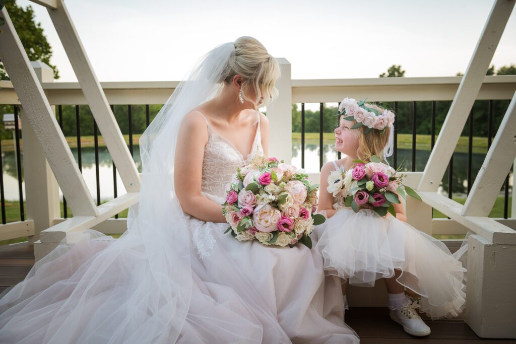 bride looking down at flower girl in front of pond