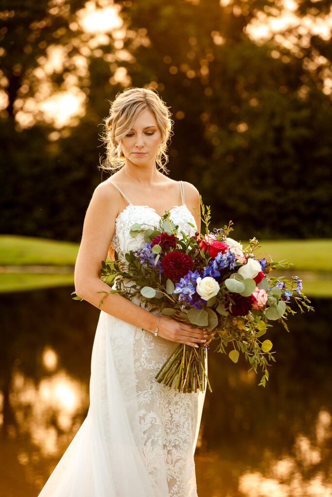 bride holding bouquet in front of pond at sunset