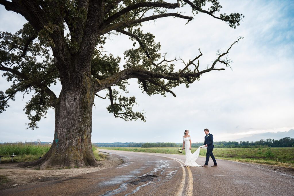 groom holding bride's dress under the Big Tree McBain, MO