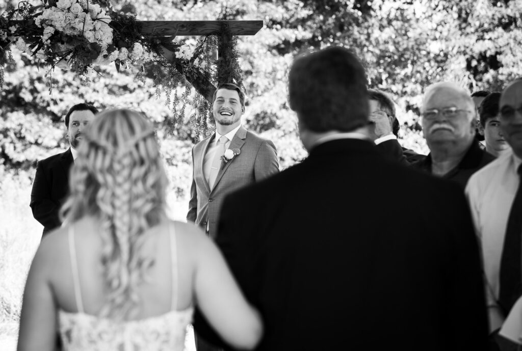 groom smiling while bride walks down aisle