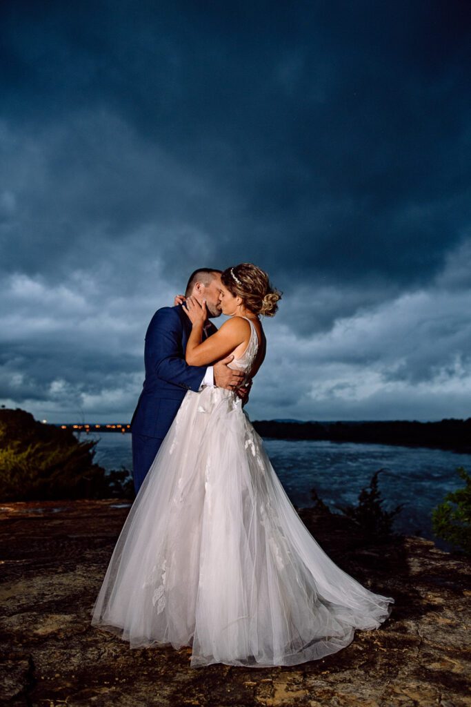 Bride and Groom kiss with dark blue storm clouds.