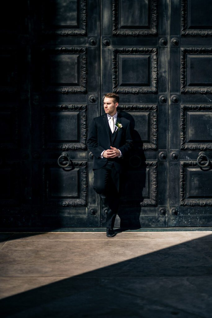 groom leans on black tall doors in suit