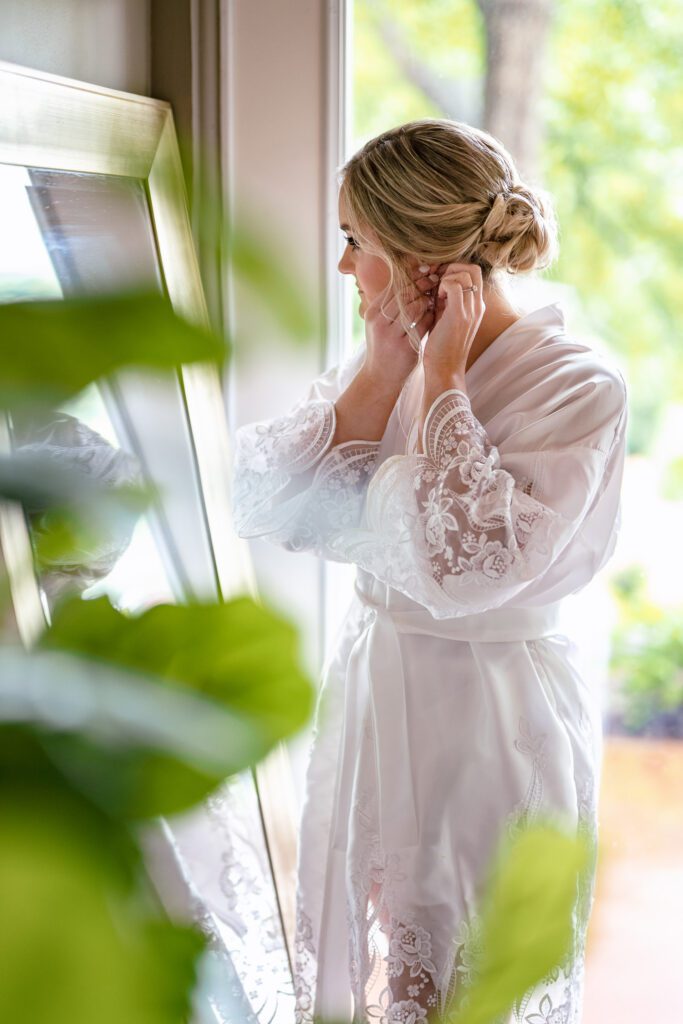 bride putting on earrings in mirro