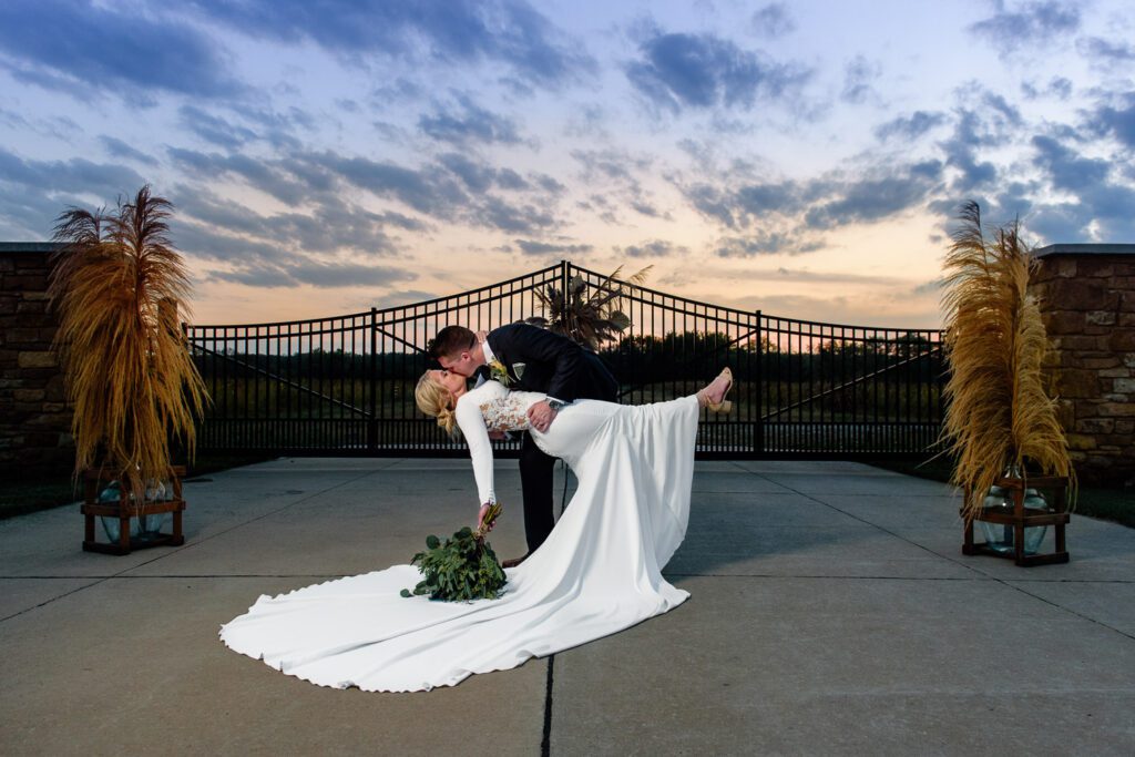 groom dipping bride in front of a gate