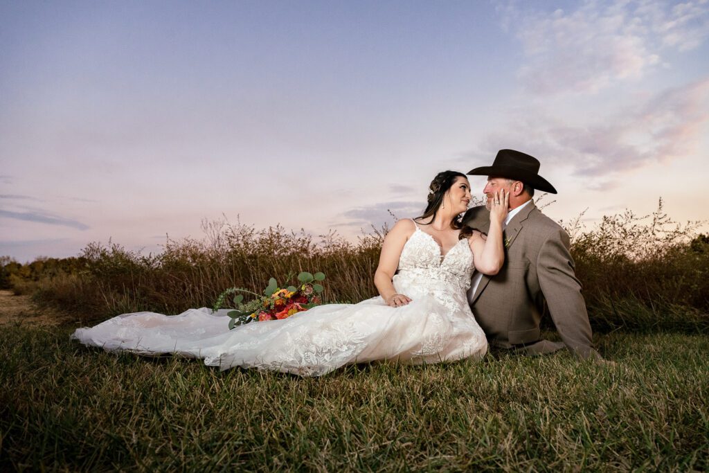 bride and groom in a field with cowboy hat