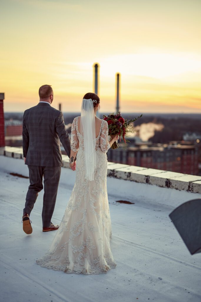 bride and groom walk across roof at sunset