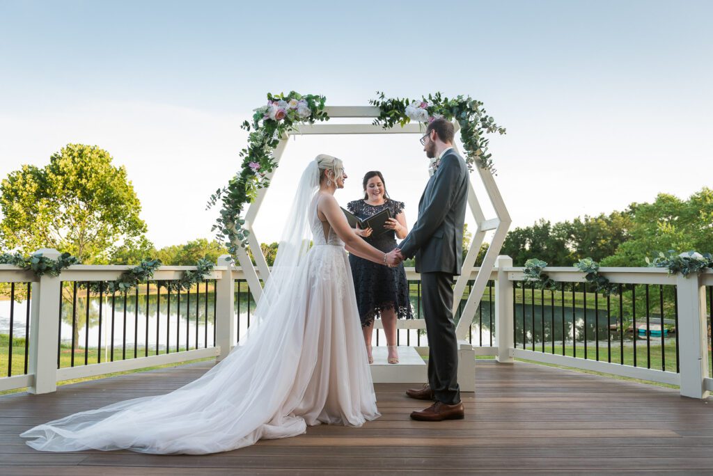 bride and groom getting married in front of floral arbor and pond Columbia, MO