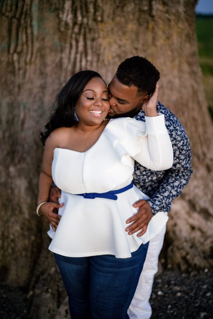 Couple snuggle in front of big tree