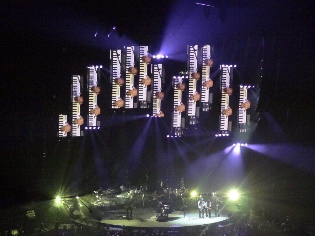 Billy Joel performs in St. Louis with multiple screens showing his hands on the piano keys.