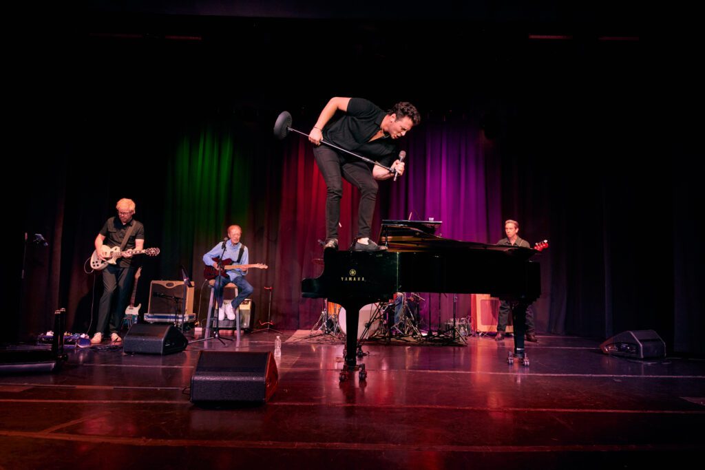 Jacob Tolliver stands on piano and sings into microphone during Jerry Lee Lewis Tribute Show