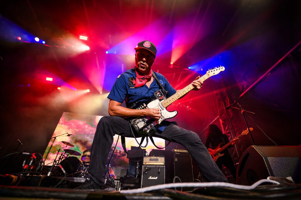 Tom Morello plays white electric guitar while looking at camera