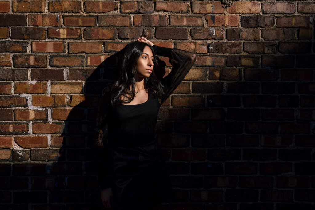 Sunlight casts shadow on senior girl leaning on brick wall