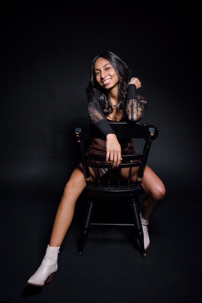 latino senior girl sits backwards on wooden chair in studio