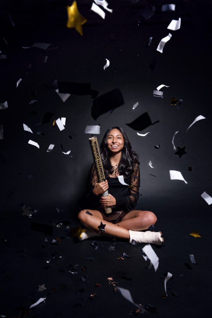Senior girl pops confetti cannon in front of black backdrop