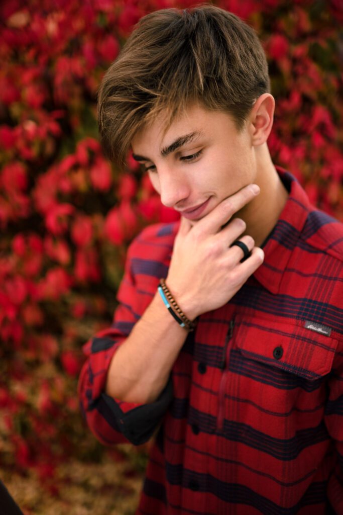 senior guy with hand on chin wearing red eddie bauer flannel in front of red burning bush