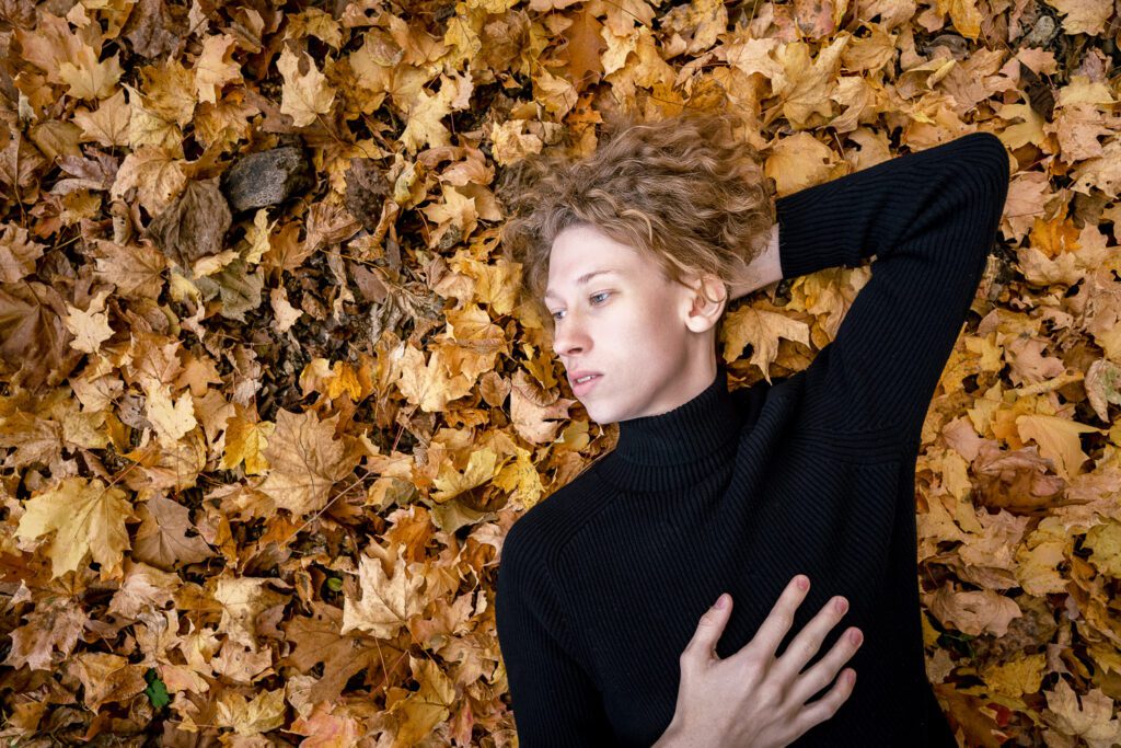 senior guy laying on pile of leaves wearing black turtle neck