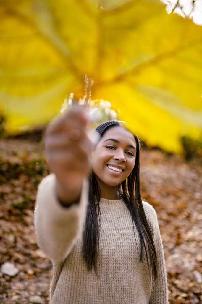 senior girl holding large yellow leaf in creek bed