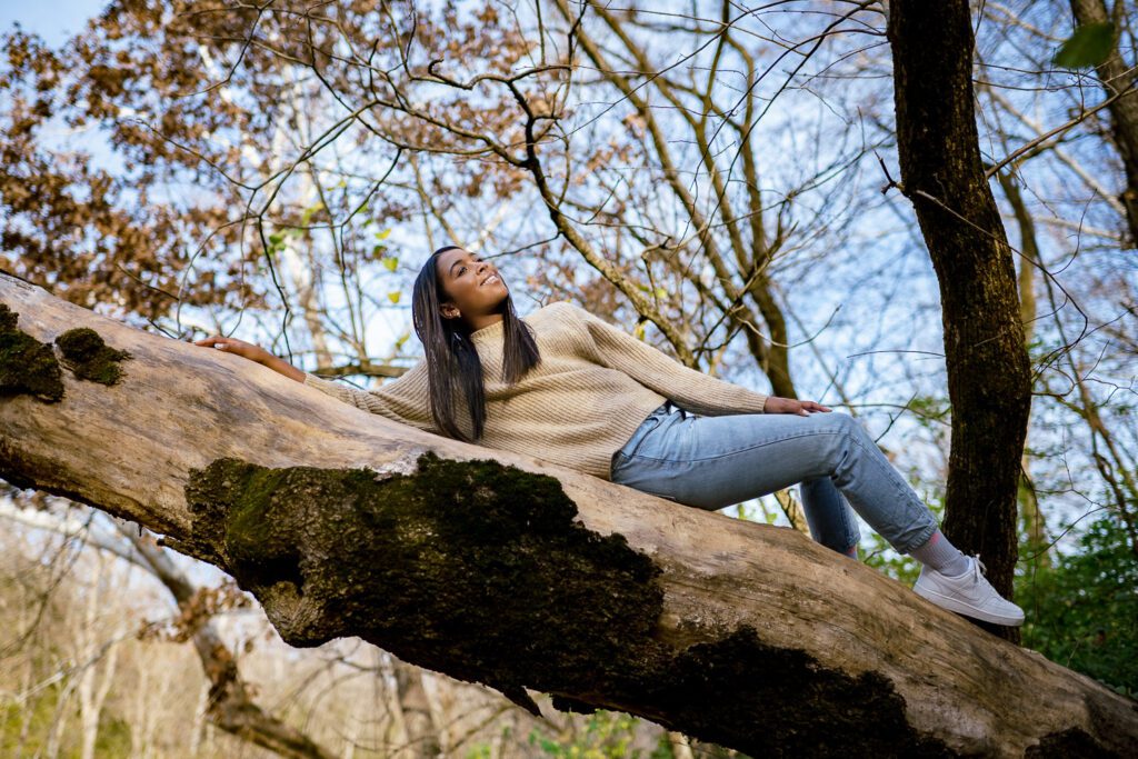 senior girl laying on tree limb above creek.