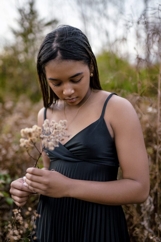 black senior girl in dress holding fall flowers in field