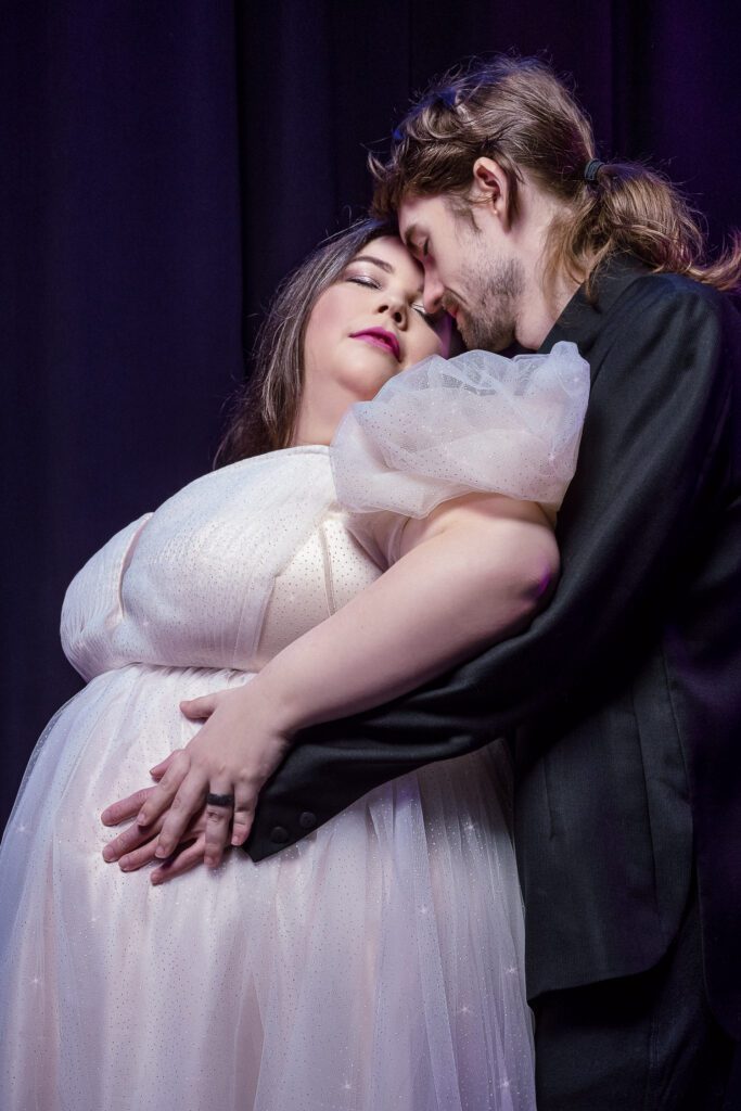 Husband and Wife snuggle together during Maternity Photos wearing formal suit and gown.