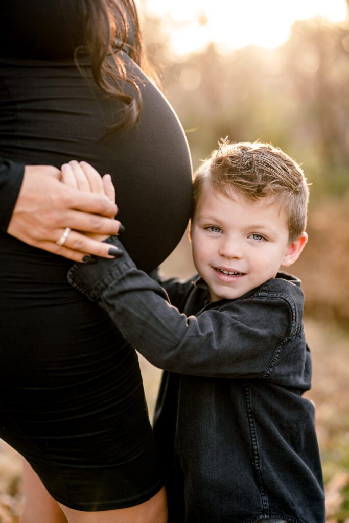 Young son snuggles to mother's pregnant belly during maternity photos.