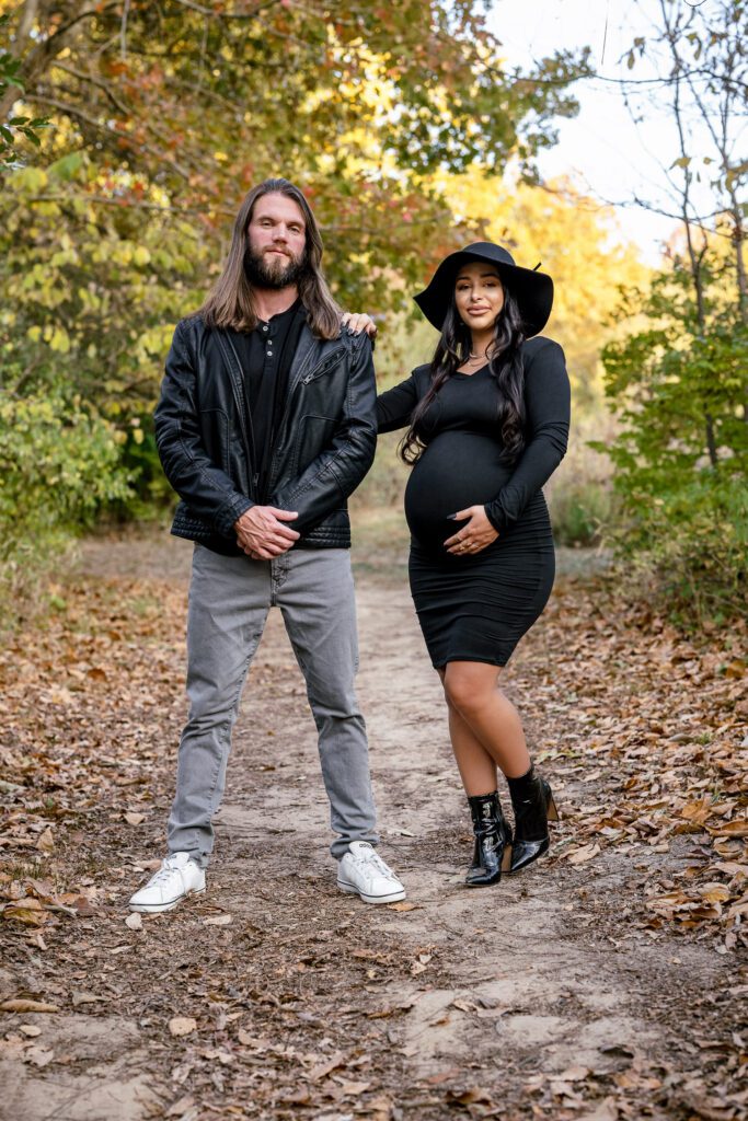 Expectant parents stand on trail wearing black.