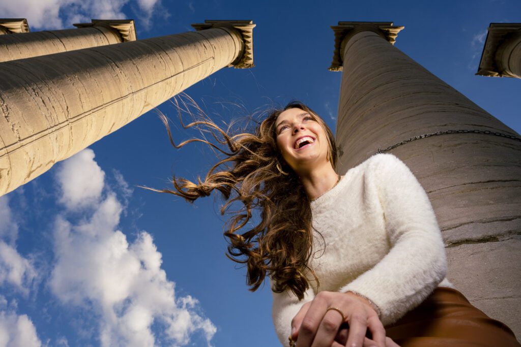 Senior girl wearing white sweater laughs while leaning forward with the Mizzou Columns in the background