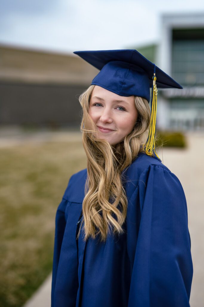 Blonde girl wearing blue cap and gown poses for senior pictures in front of Battle High School in Columbia, Missouri
