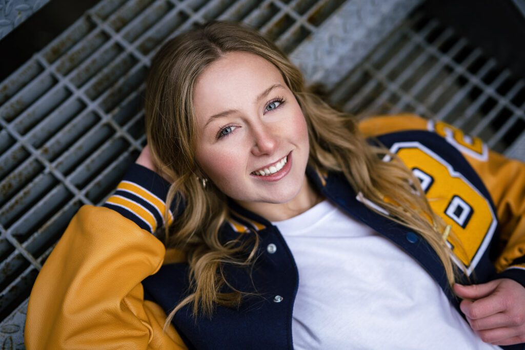 senior girl lays on staircase wearing letter jacket for Battle High School in Columbia Missouri