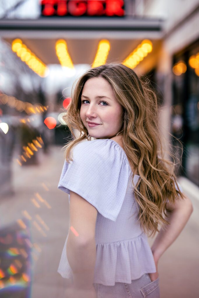 Senior girl looks over should with tiger hotel lights downtown