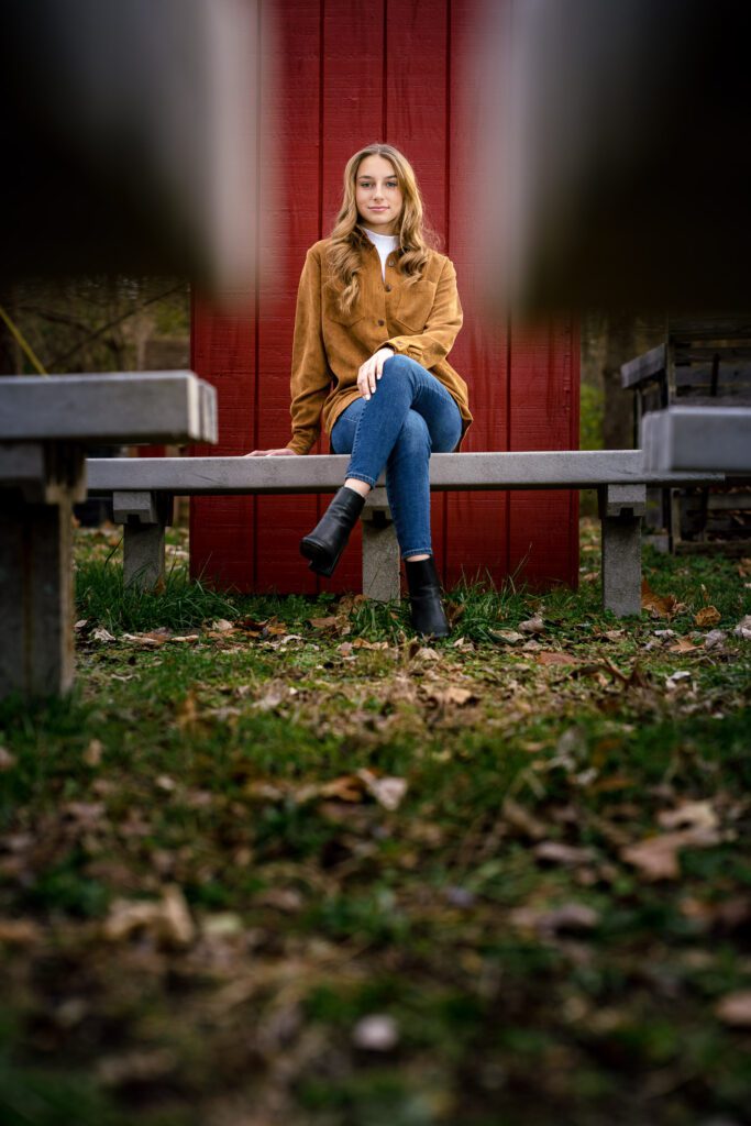 senior girl sitting on bench in front of red shed