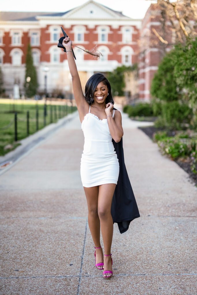 Black mizzou college senior girl raises graduation cap in air and holding gown as she walks down sidewalk