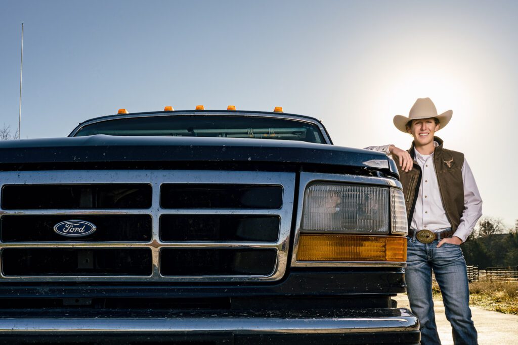 Senior guy wearing cowboy hat and vest leans on fort pickup truck