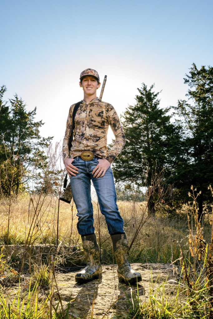 Senior guy poses in camo in field with shotguy for senior photographs