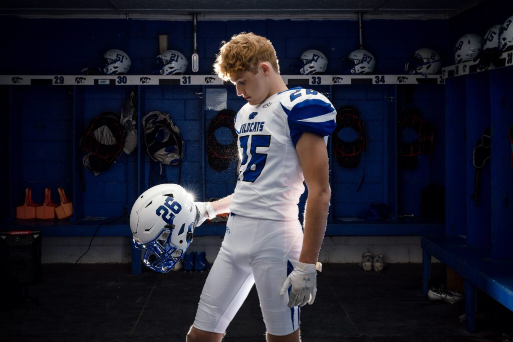 High school football player with red hair wearing Montgomery County R-II uniform looks at helmet