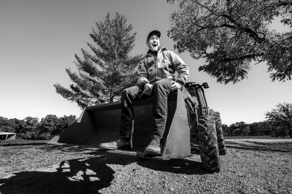 High school senior guy sitting in the scoop of John Deere Tractor laughing