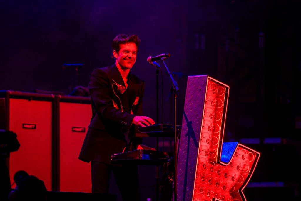 Brandon flowers smiles while playing keyboard under red light