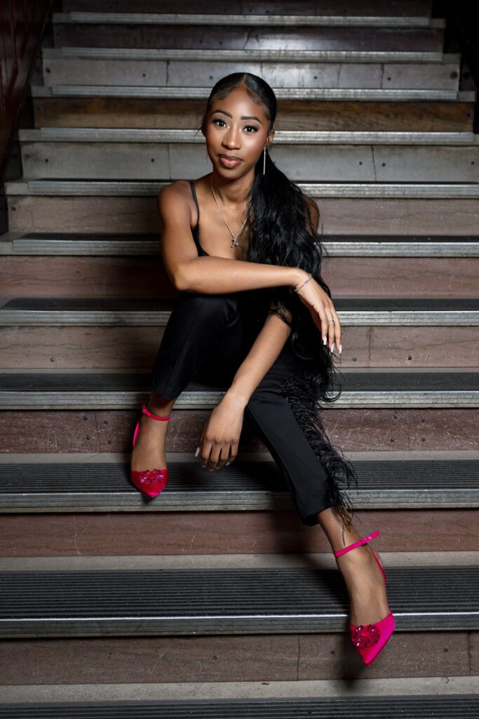 black woman wearing pink high heels relaxing on steps wearing black outfit