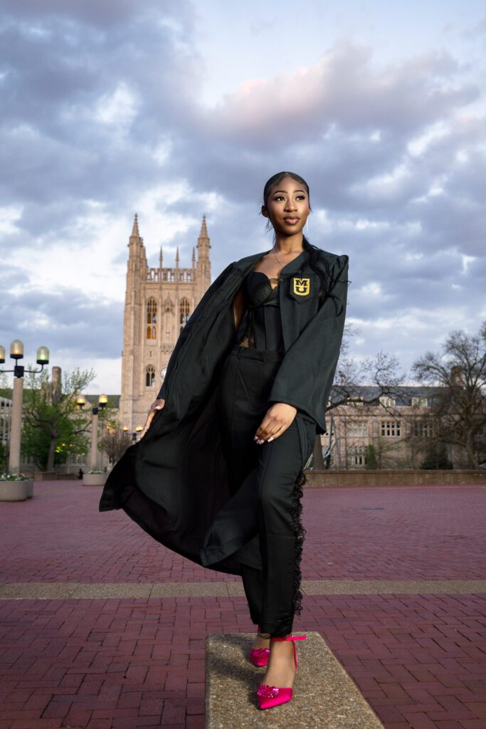 Black senior girl wearing black graduation gown and pink high heels in front of Memorial Union tower