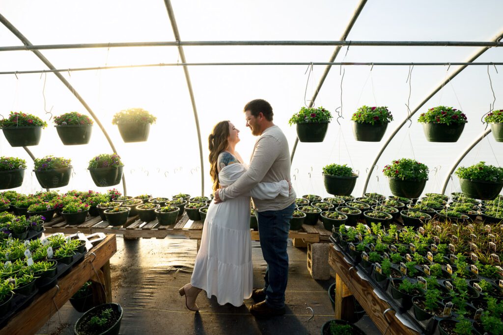 engaged couple hugging and looking at each other in green house with hanging plants
