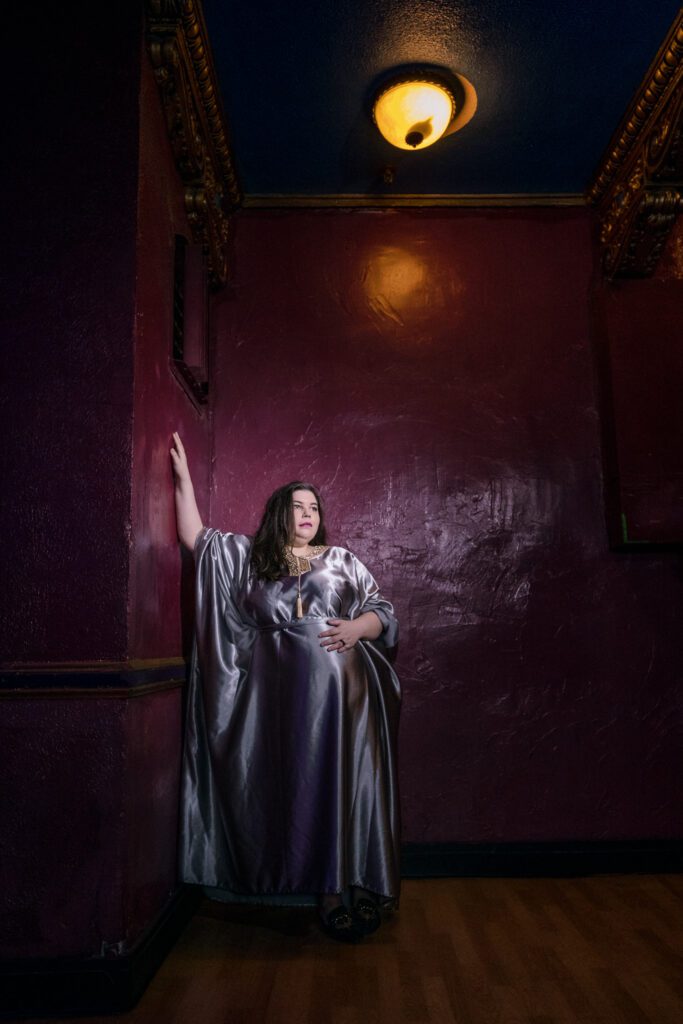 Maternity photo shoot at the Blue Note in Columbia Missouri with a silver maternity dress. Mom to be leaning on wall.