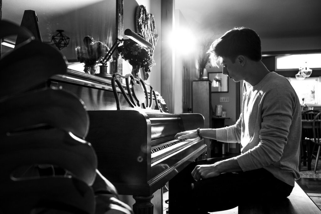 senior guy playing piano in back lit black and white photo