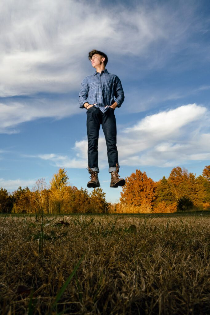 Senior guy appears to be floating in front of fall trees in field