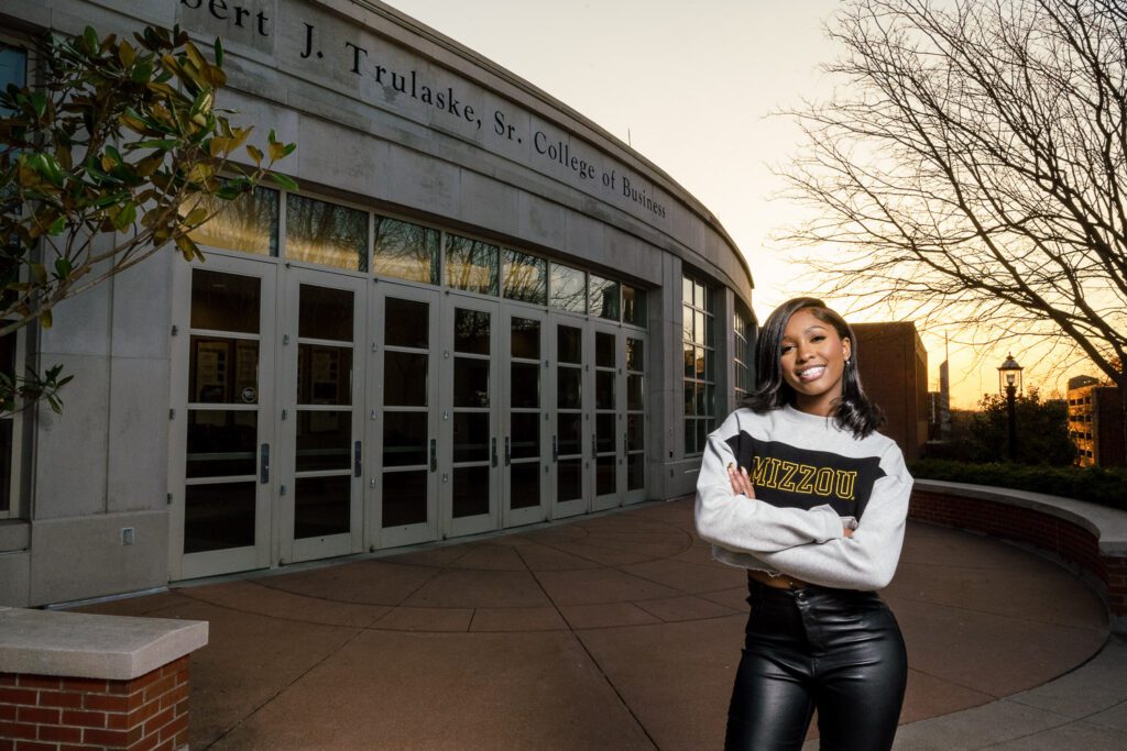 College Senior Girl with arms crossed standing in front of building.