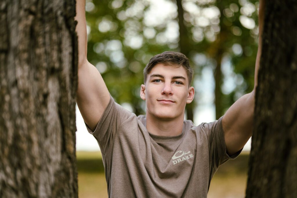 High School senior wrestler flexes biceps arm muscles between two trees